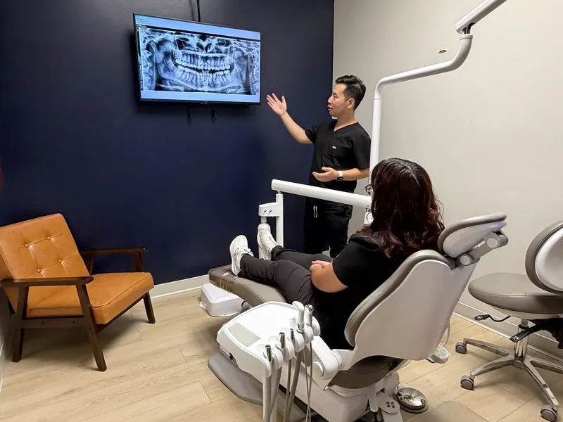Dr. Tam points to a panoramic X-ray on the wall screen as a patient watches from the chair